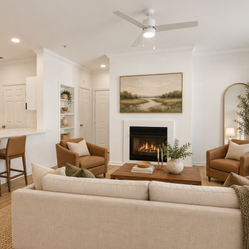 Open-concept living room with a fireplace, neutral sofa, and large windows flowing into the kitchen at The Ashborough apartments in Ashburn, VA